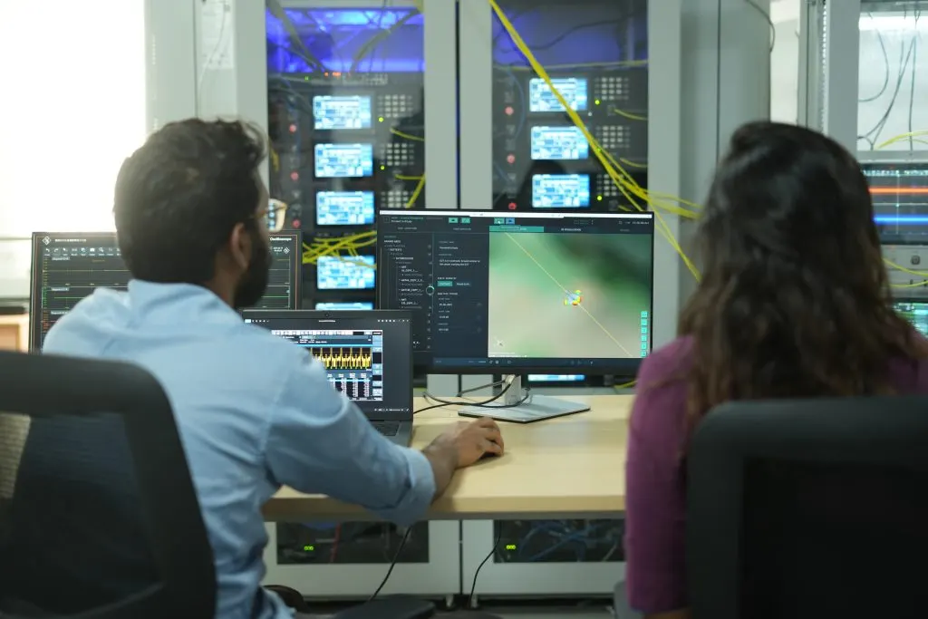 Two engineers at a Constelli electronic warfare test bench, working at operator consoles in front of a rack of instrumentation